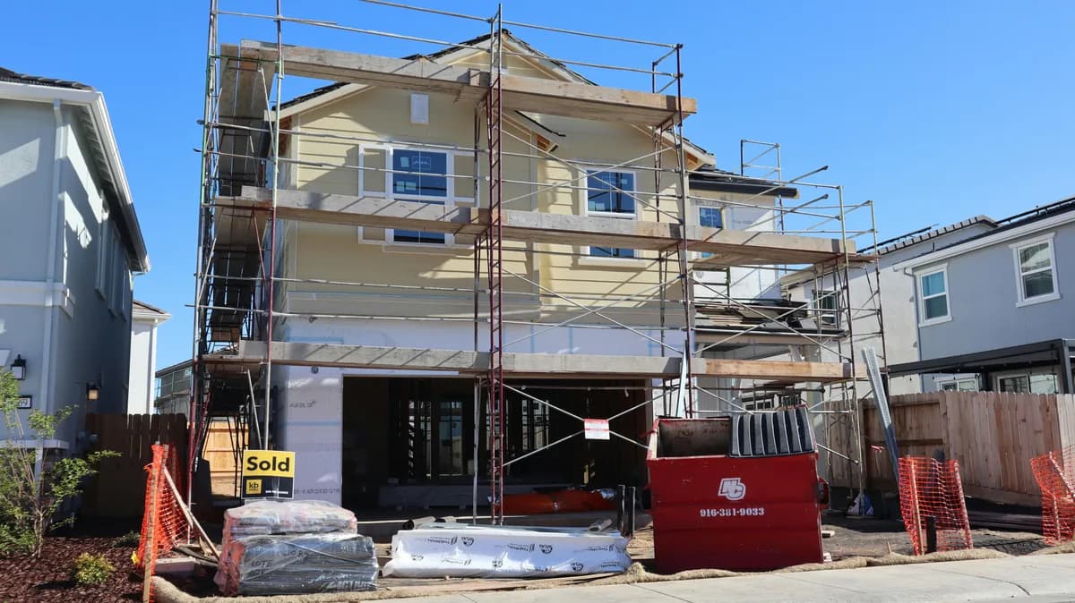 Multi-story residential home under construction with protective scaffolding and building materials