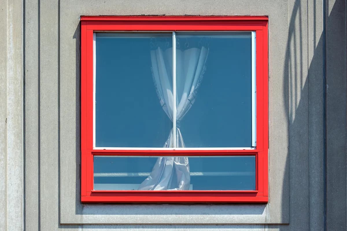 Bright red window frame with sheer curtains visible through clean glass panes