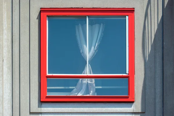 Bright red window frame with sheer curtains visible through clean glass panes