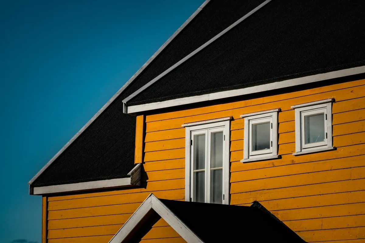 Modern yellow house with white-framed windows and black roof against clear sky