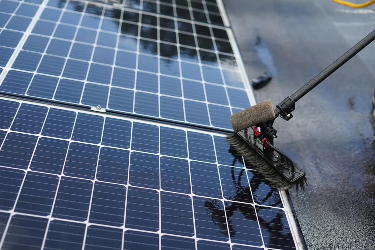 Professional cleaning brush washing solar panel surface with squeegee tool