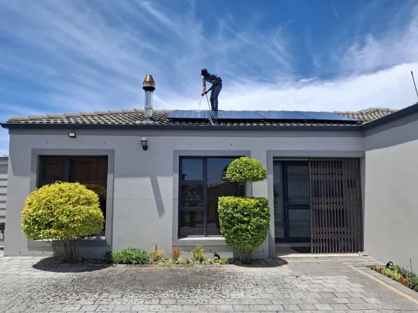 Worker on residential roof installing blue solar panel systems under clear sky