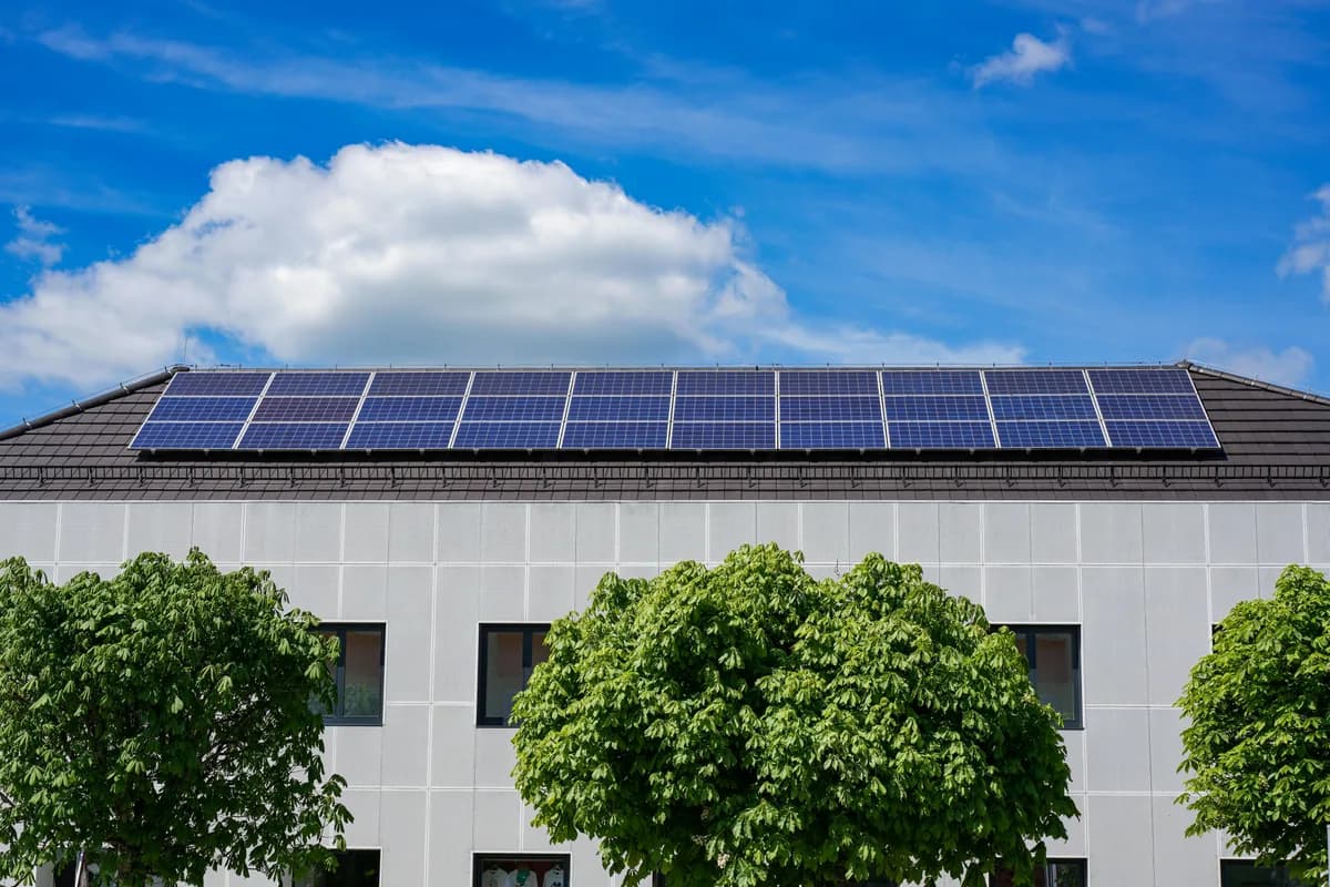 Modern white building with solar panels on roof and green trees in front
