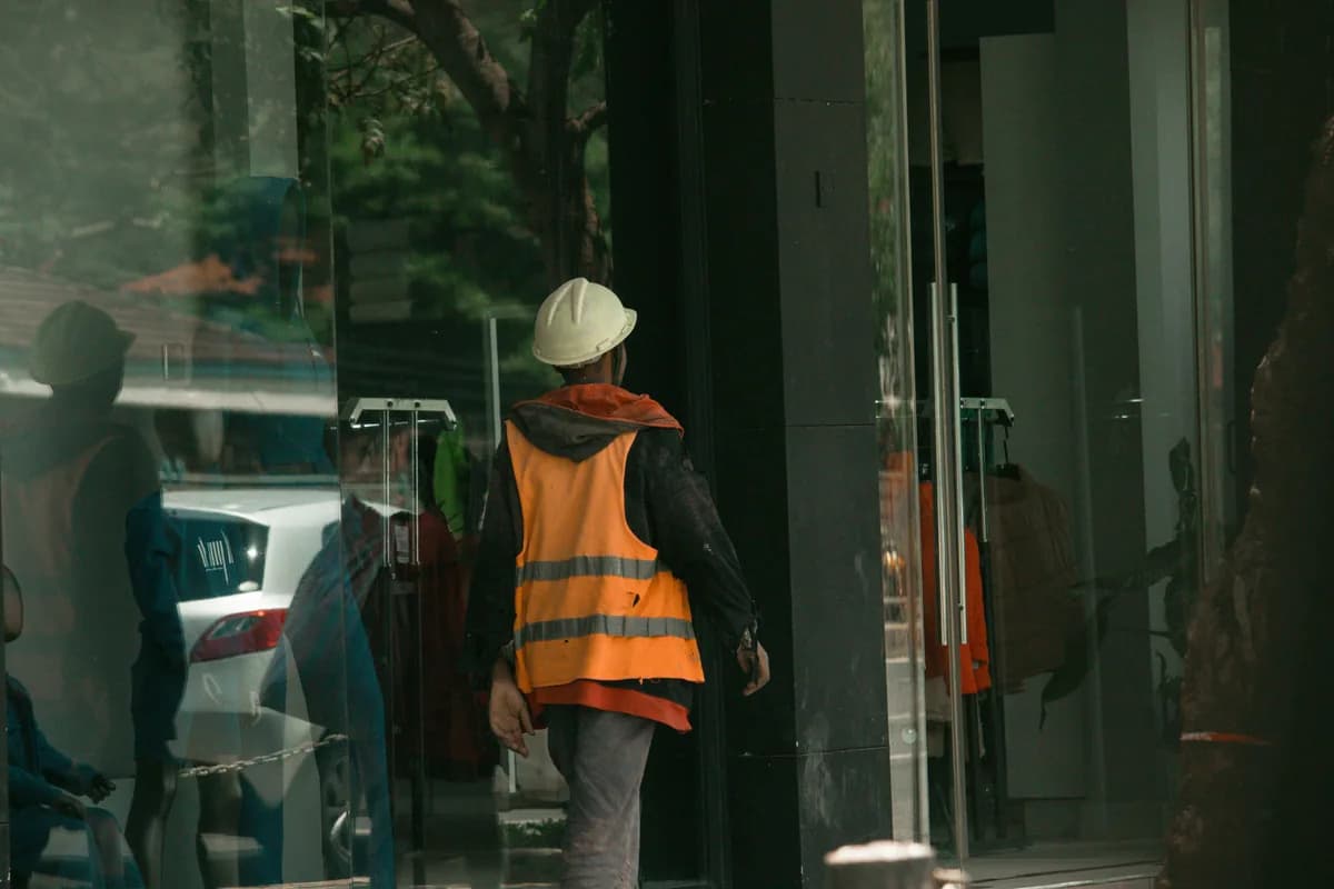 Construction worker in safety vest and hard hat entering glass building entrance