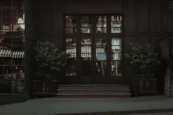 Dark storefront with large glass doors and windows, potted plants flanking entrance
