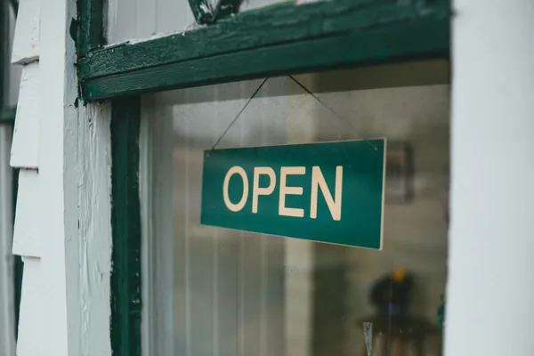 Green open sign hanging on glass door of storefront entrance