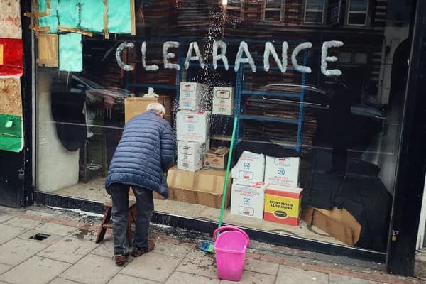 Person cleaning storefront window with water and pink bucket outside