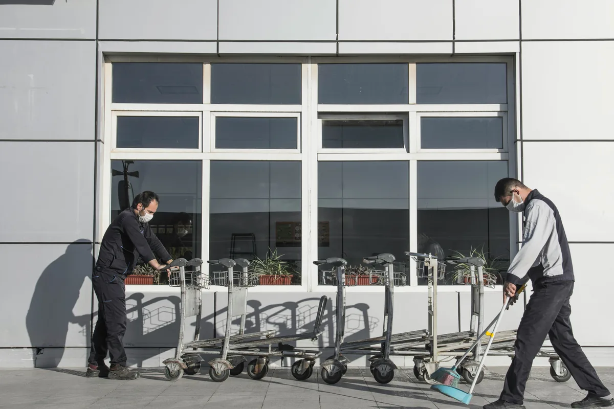 Two workers sweeping pavement in front of modern building with large windows