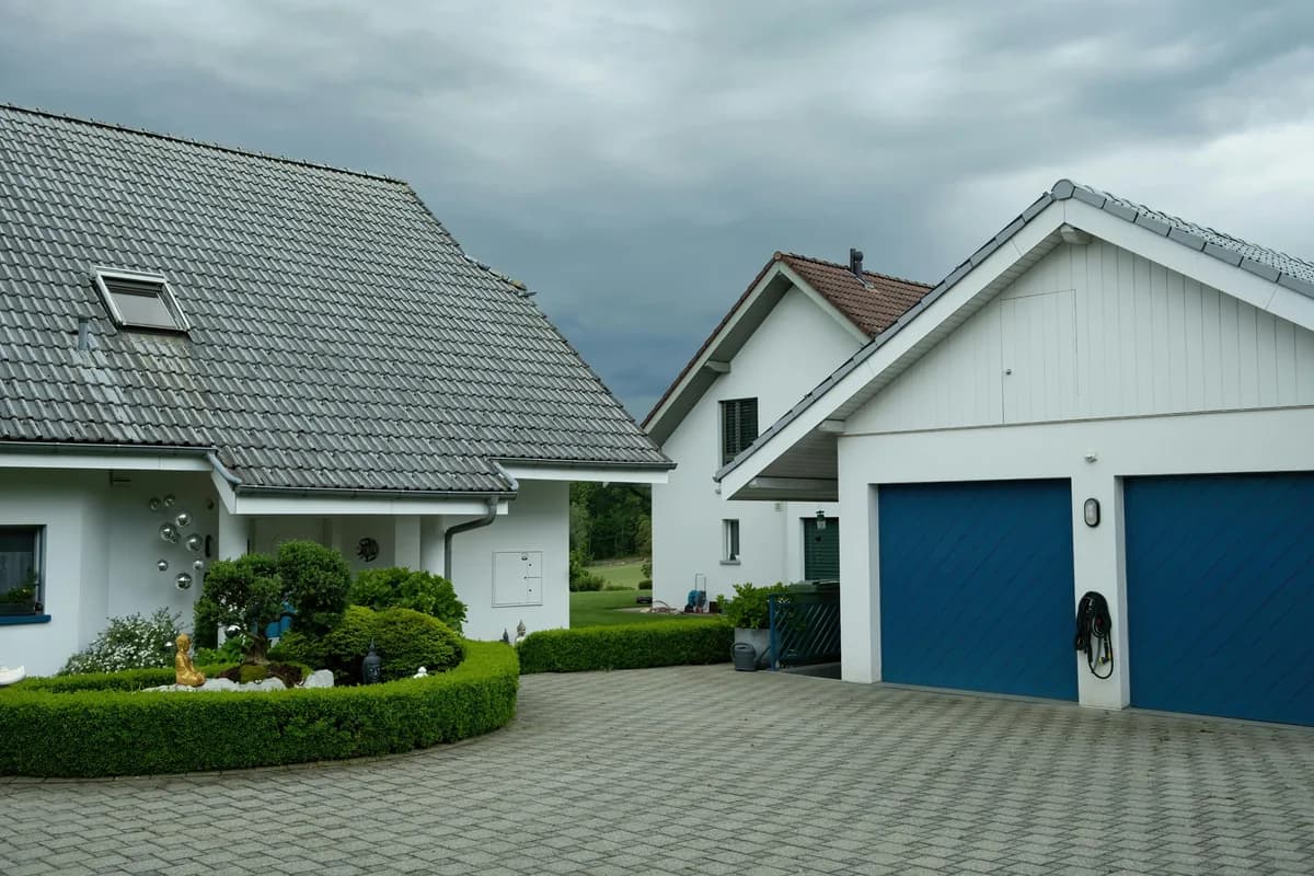 Modern white residential home with manicured landscaping and blue garage doors