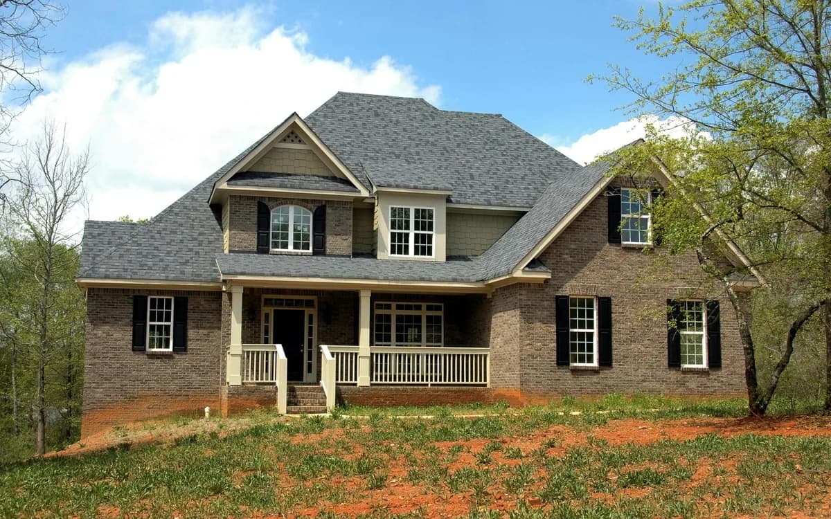 Two-story brick house with white porch and black shutters on landscaped grounds