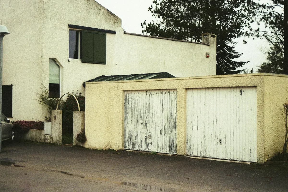 Modern residential building exterior with two weathered white garage doors
