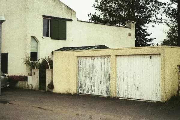 Modern residential building exterior with two weathered white garage doors