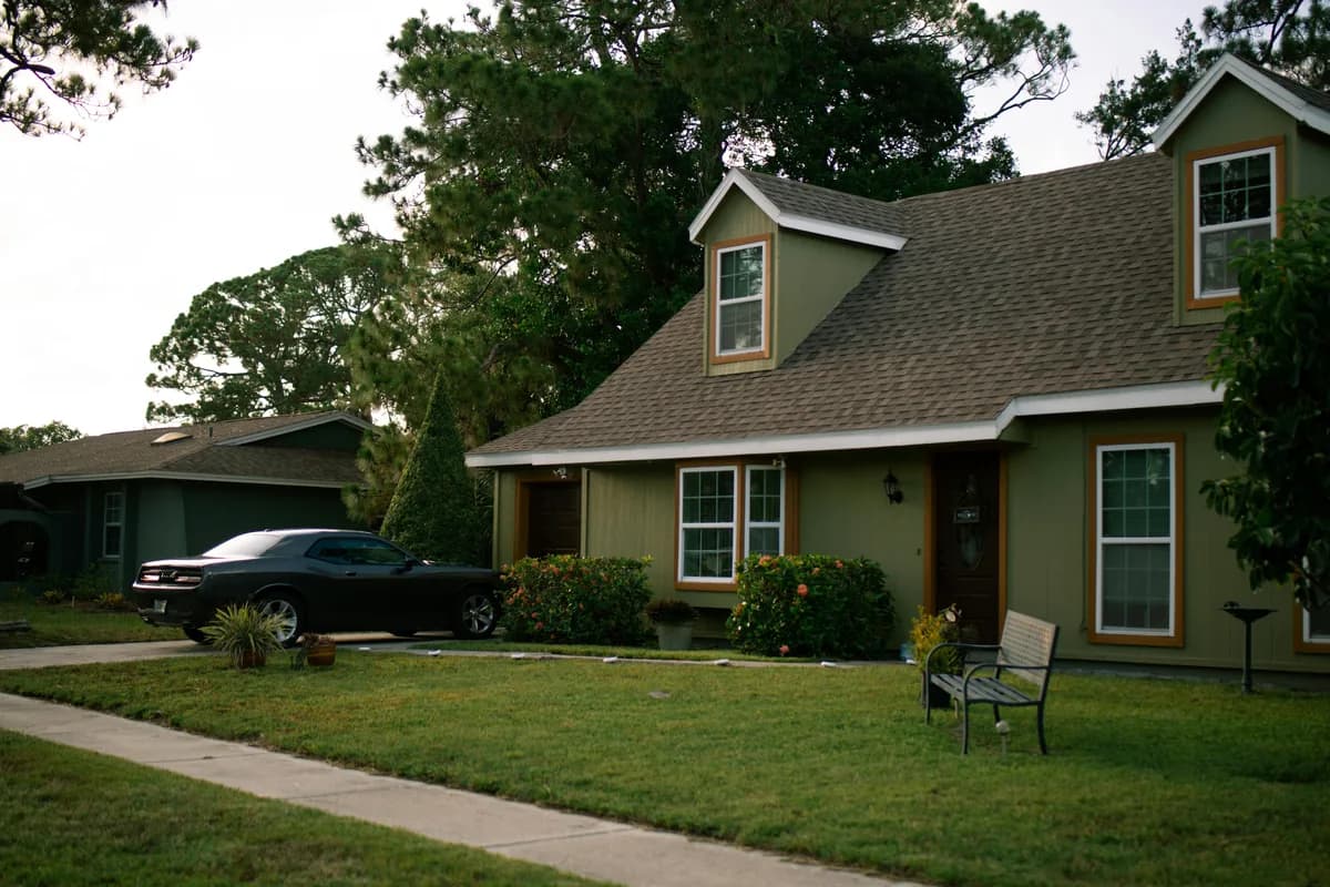 Green residential home with large windows and attached garage among trees