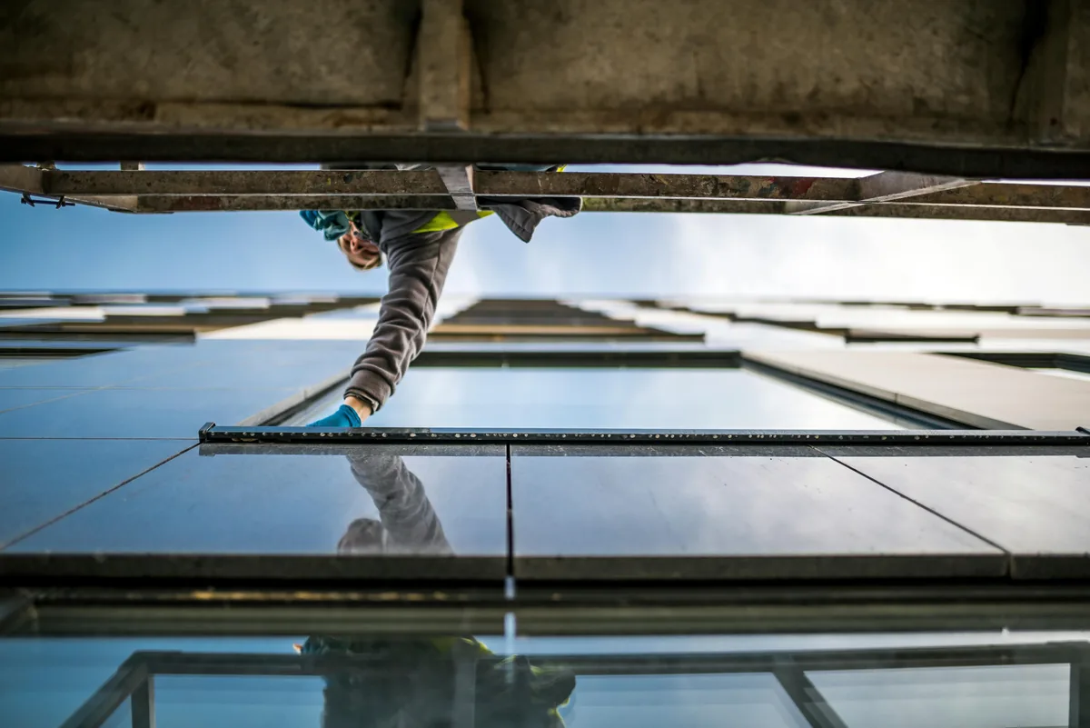 Worker cleaning large exterior windows on tall building facade with clear sky