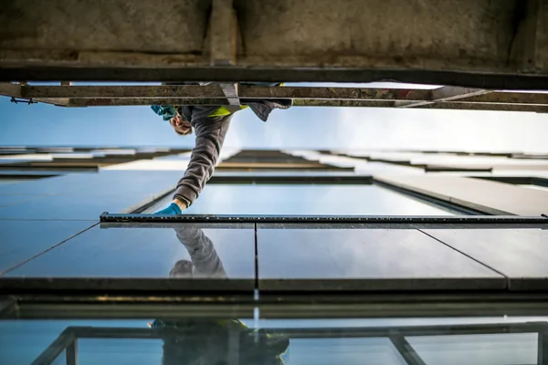 Worker cleaning large exterior windows on tall building facade with clear sky