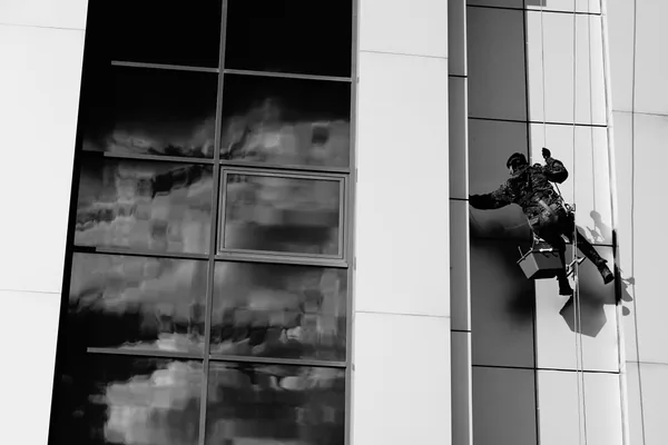 professional window cleaner rappelling down modern glass building facade