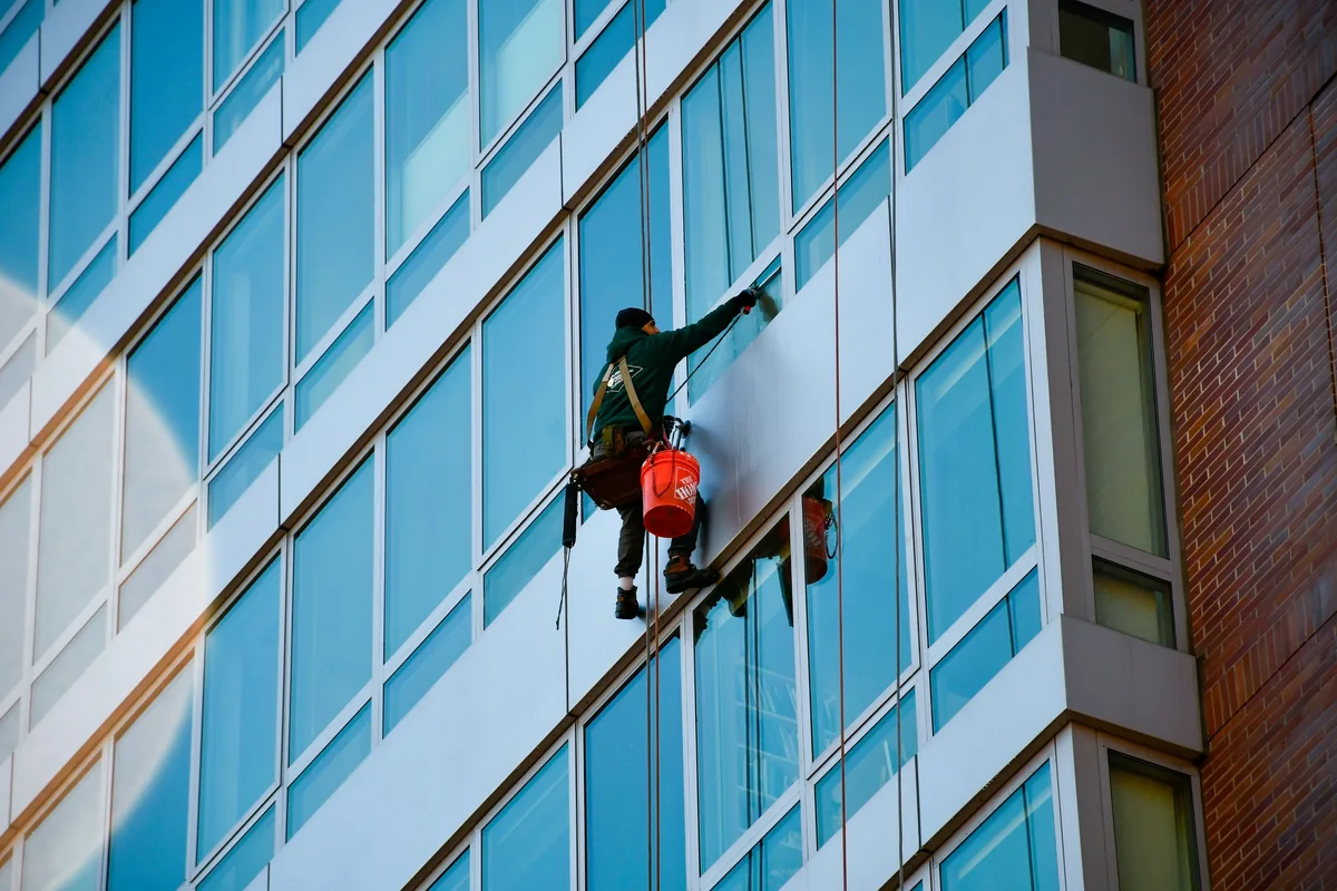 professional window cleaner rappelling down modern glass building facade